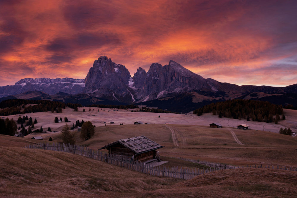 Un chalet dans les alpes de siusi avec un ciel orange pendant le sunrise.