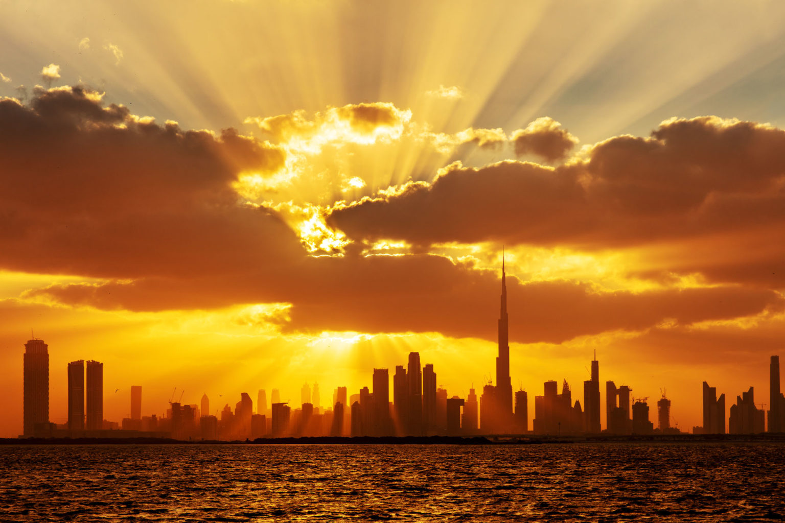 La skyline de Dubaï au sunset avec des rayons de soleil qui percent les nuages.