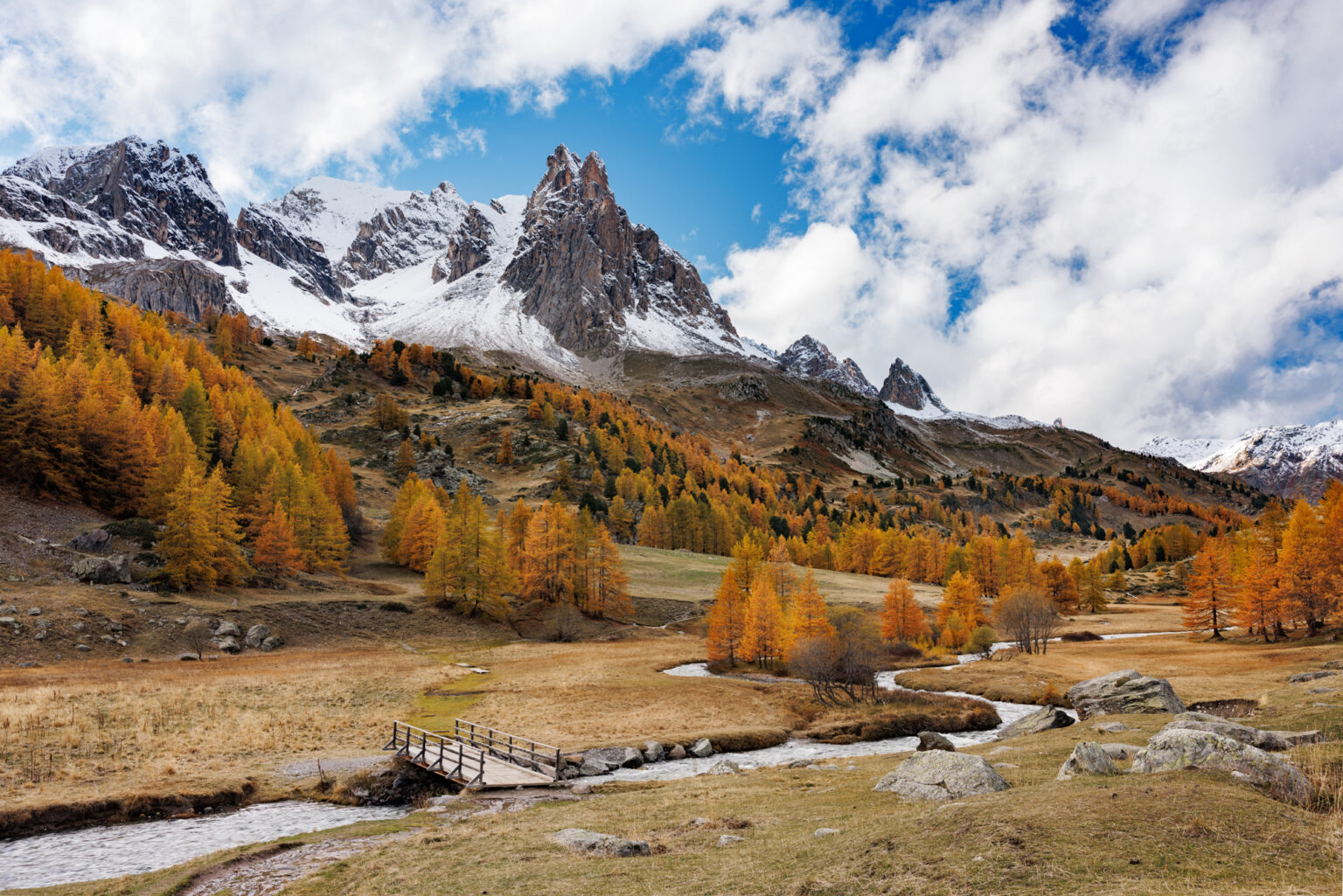 La haute vallée de la Clarée en automne avec un pont en bois, de la neige sur les montagnes et les mélèzes rouges.