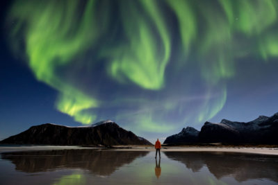 Aurore boréale au-dessus d'un personnage sur la plage de Skagsanden (îles Lofoten en Norvège).