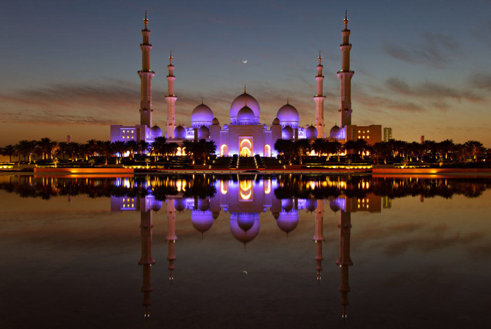 La mosquée cheikh zayed à abu dhabi avec son reflet et un croissant de lune.